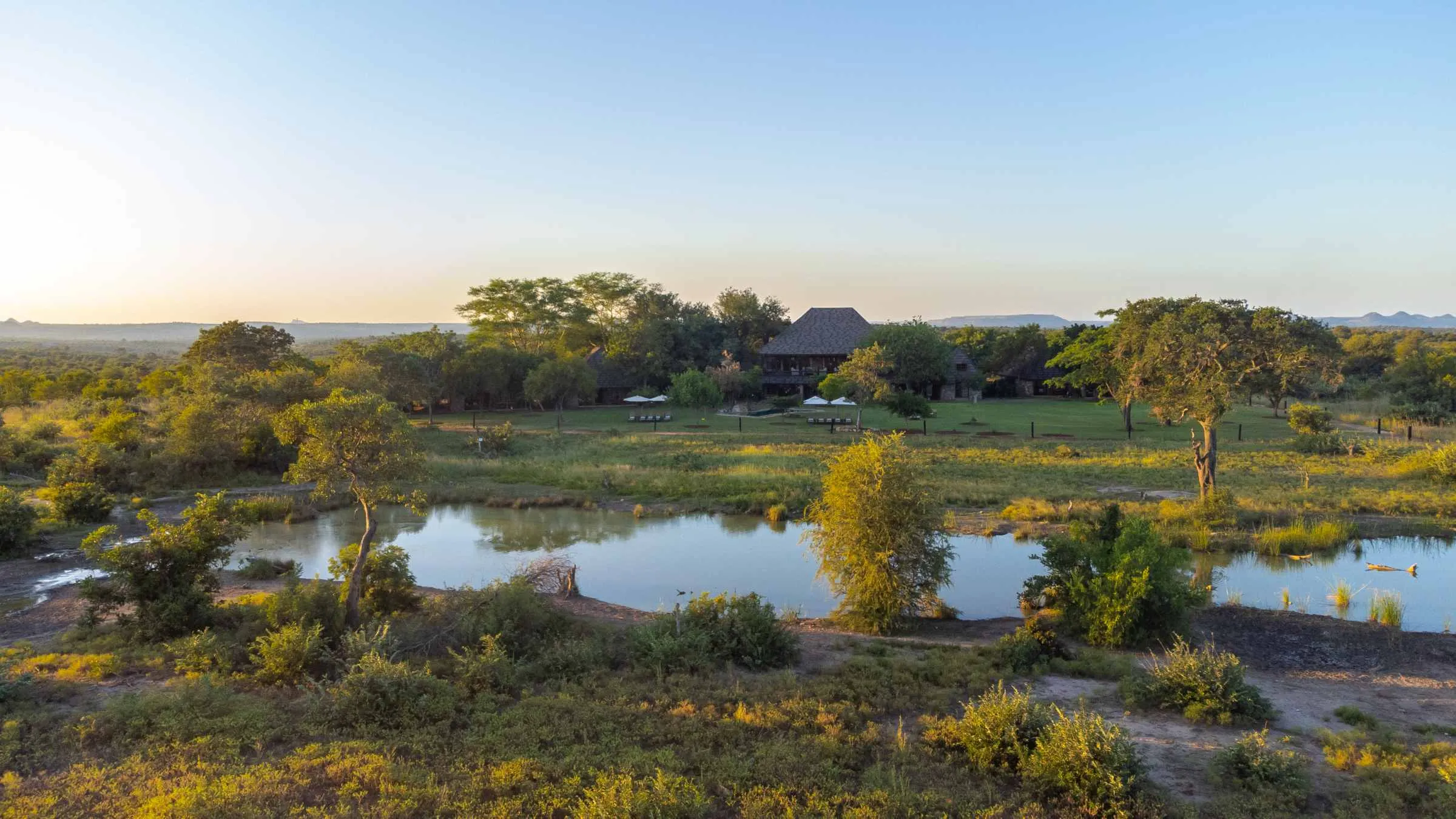 Aerial view of Nzumba Lodge's chalets and waterhole at golden hour in Klaserie Private Nature Reserve