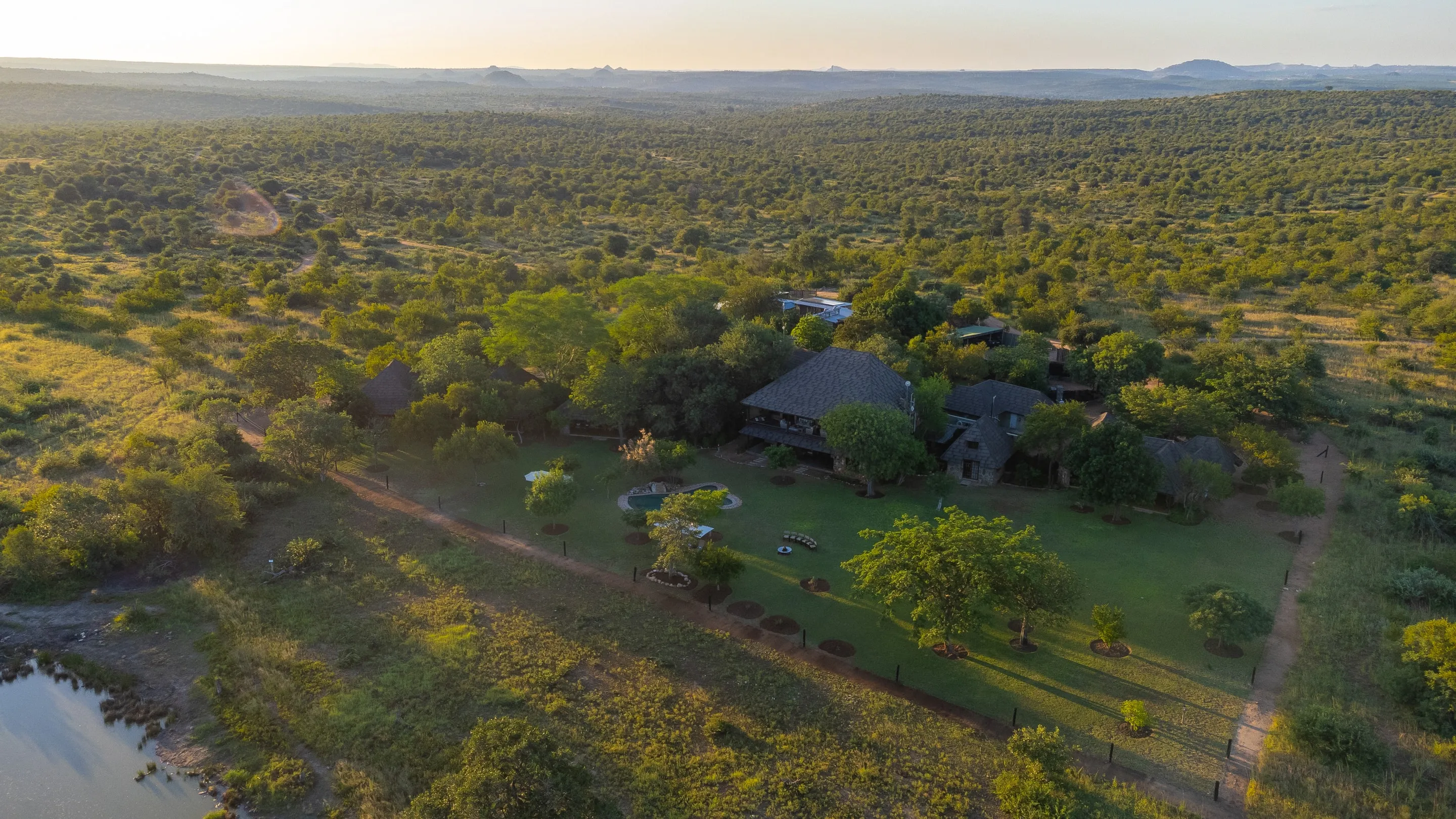 Aerial view of Nzumba Lodge's chalets and waterhole at golden hour in Klaserie Private Nature Reserve