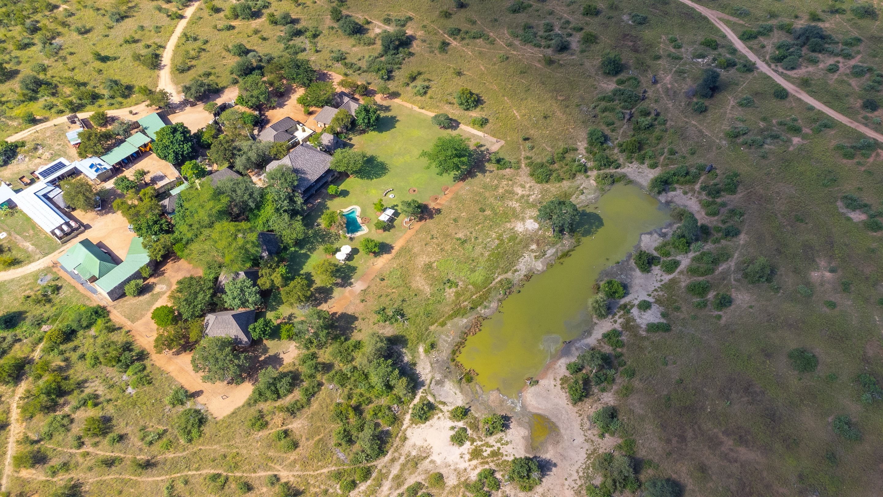 Overhead aerial view of the Nzumba Lodge chalets clustered beside the green waterhole