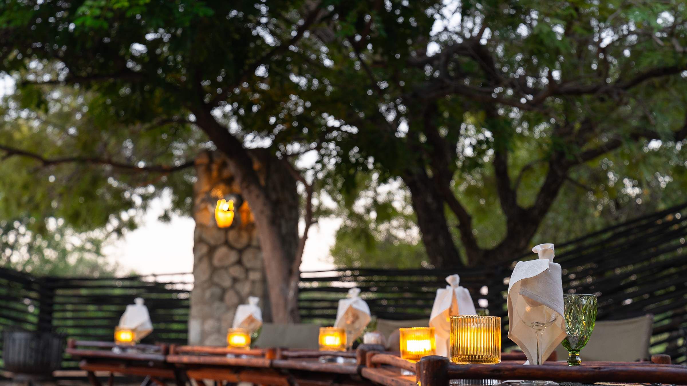 Nzumba Lodge main building, boma firepit and pool at golden hour, framed by acacia trees