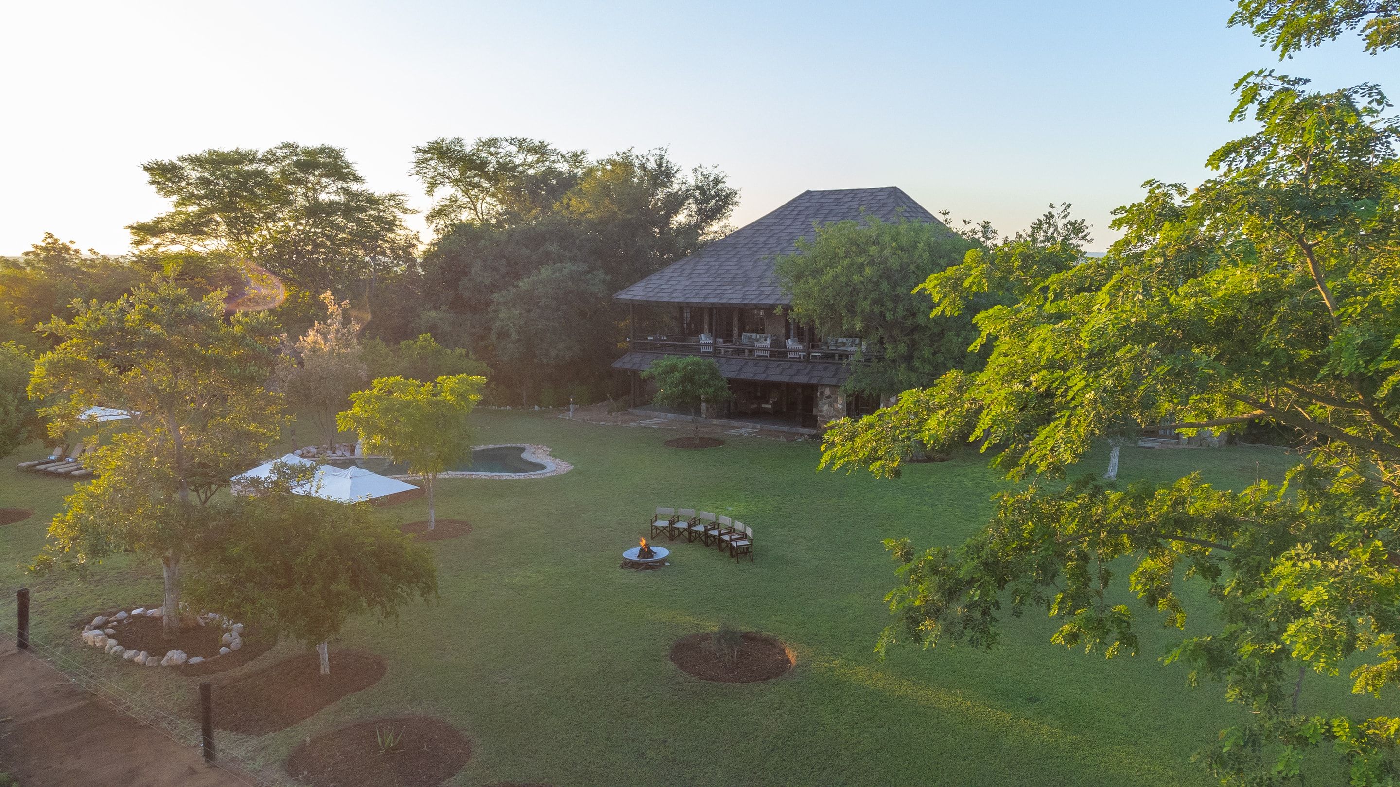 Nzumba Lodge main building, boma firepit and pool at golden hour, framed by acacia trees